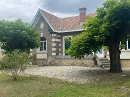Une maison girondine derrière deux arbres feuillus.